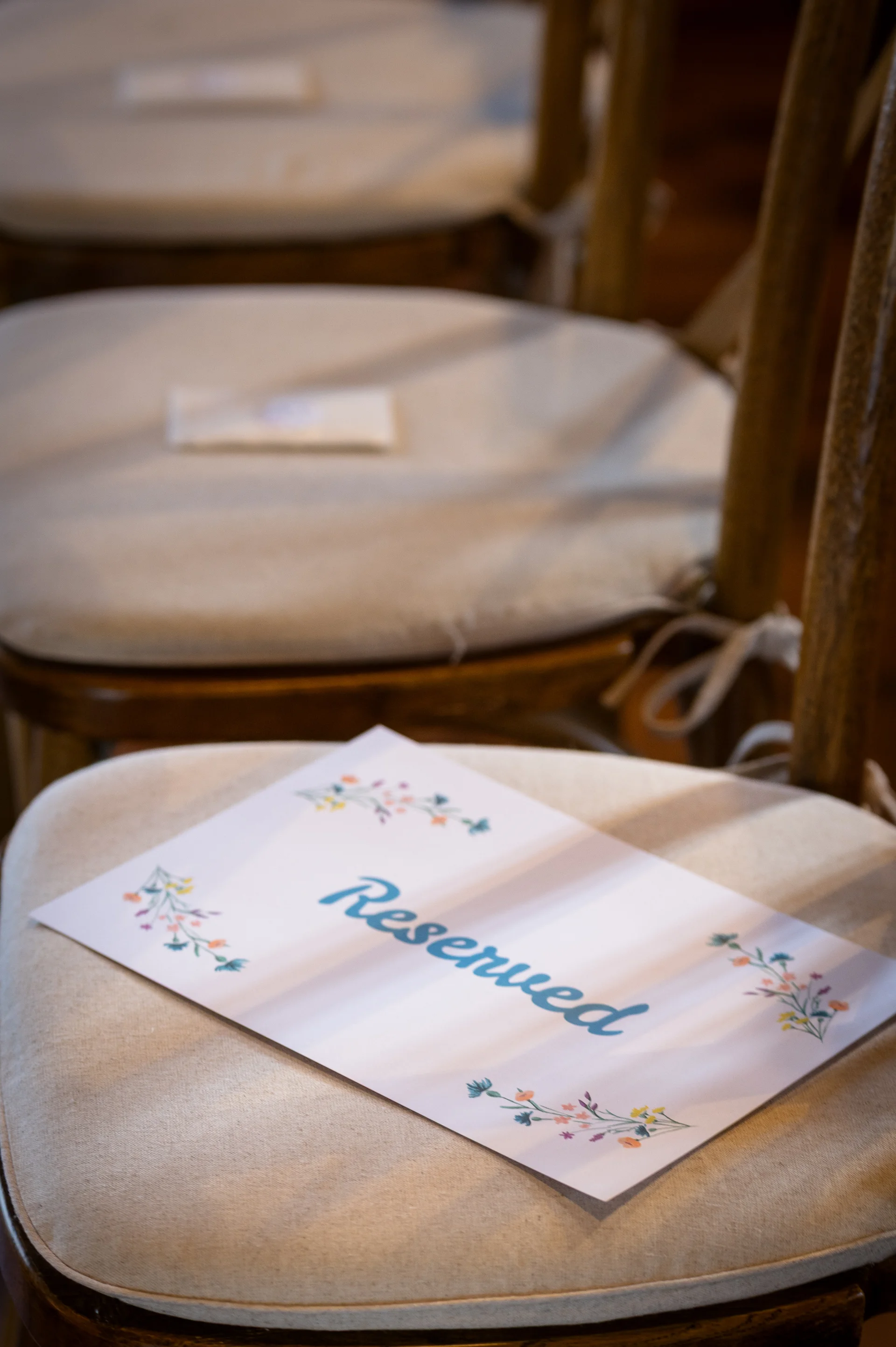 A reserved sign with delicate floral illustrations and blue calligraphy rests on a padded wooden ceremony chair.