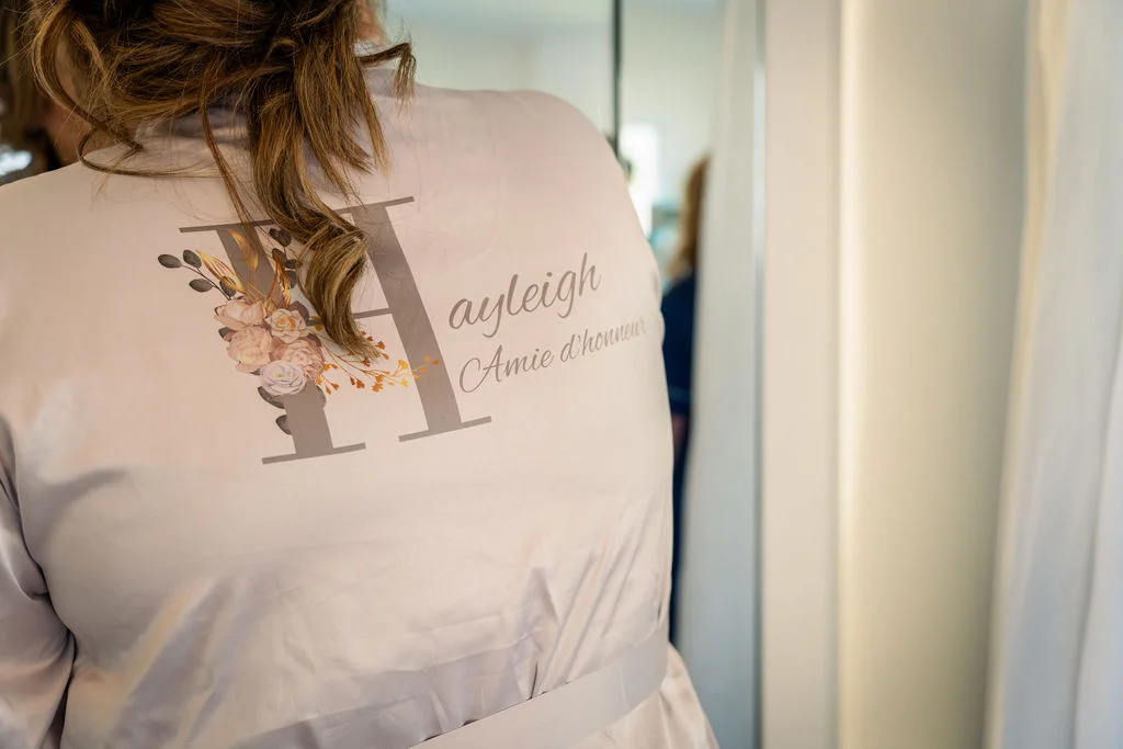 A close-up back view of a person wearing a personalised getting-ready robe featuring floral text details during bridal morning preparations.
