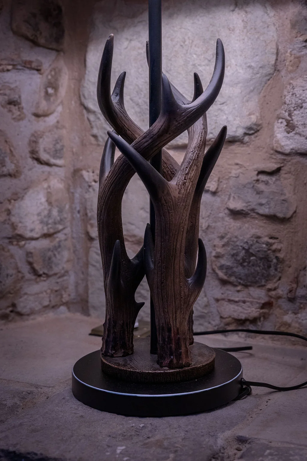 Close-up of a rustic antler-themed lamp base standing against an exposed stone wall inside a wedding venue.