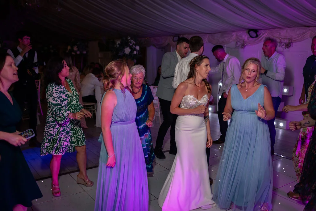 The bride in a strapless white gown and her guests happily dance on a illuminated dance floor under atmospheric purple lighting during the evening reception.