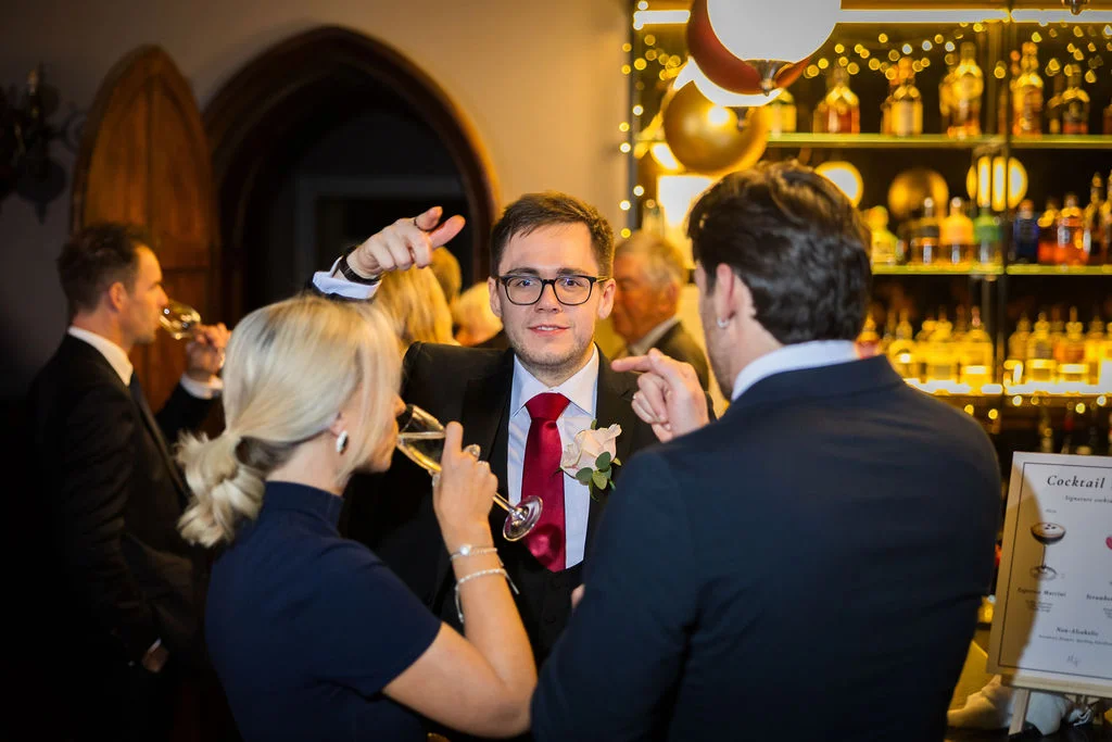 Wedding guests enjoy drinks and conversation in a warmly lit bar area during the evening reception.