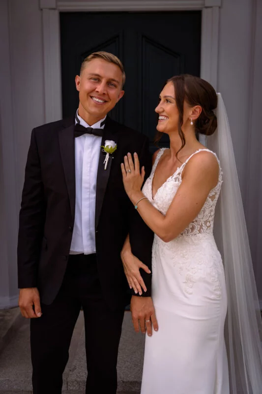 A bride and groom smiling in front of a door.