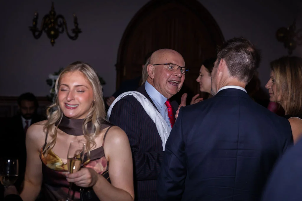 Wedding guests laugh and mingle together during a lively indoor evening drinks reception.