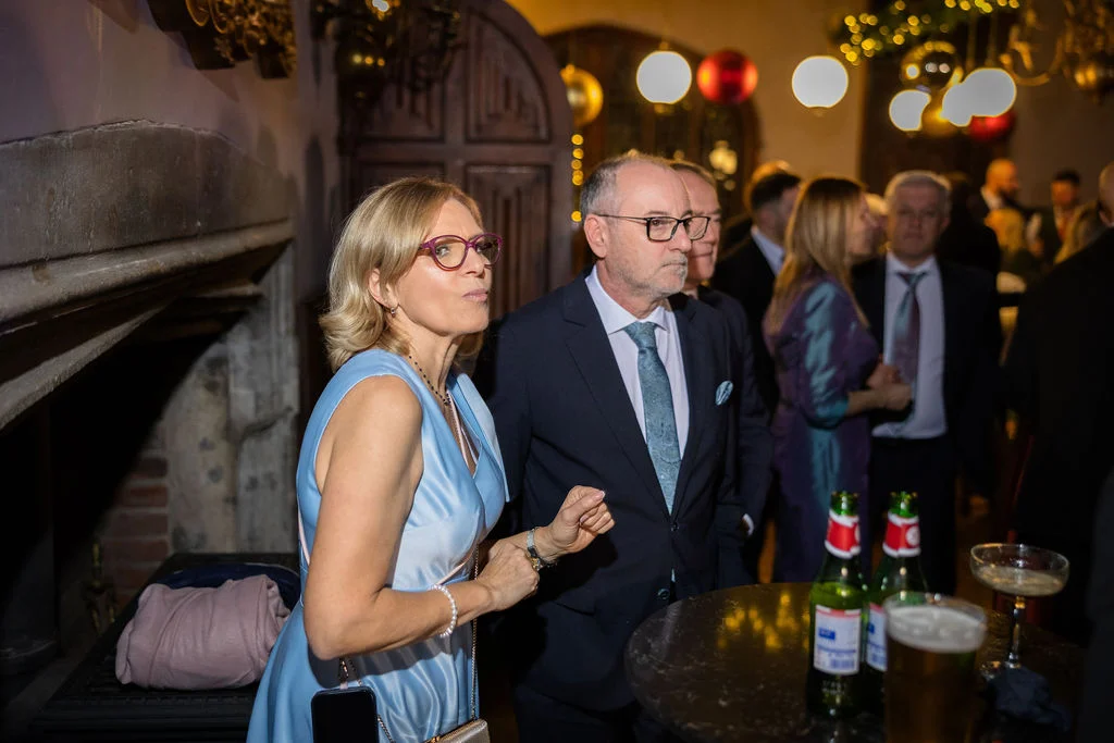Guests mingle and converse during a lively evening wedding reception inside a warm and festively lit venue.