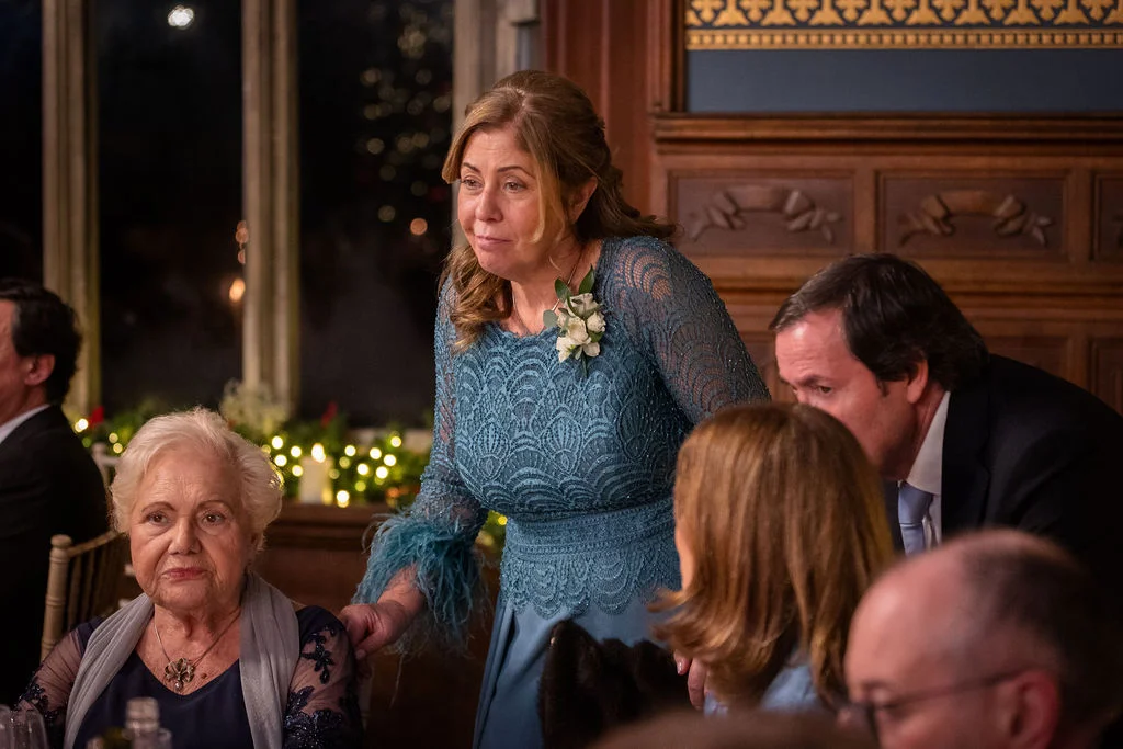 An emotional mother of the bride stands at a banquet table during wedding speeches inside a wood-panelled country house reception venue.