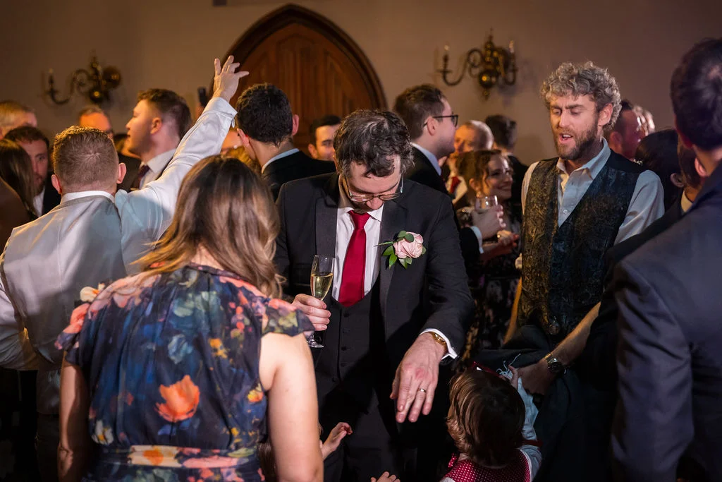 Guests enjoy a lively evening reception, with a groom in a dark suit and red tie laughing alongside dancing attendees.