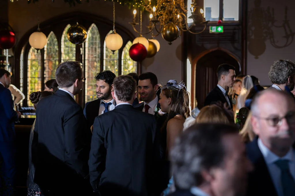 A candid shot of wedding guests mingling in a grand hall decorated with festive Christmas ornaments and warm lighting.