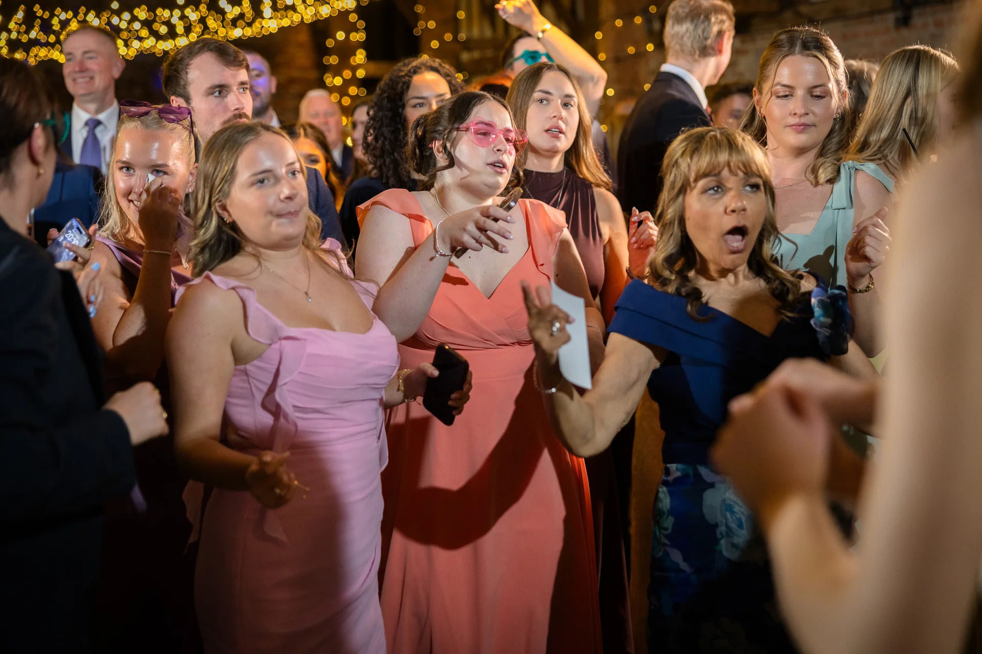 A lively group of wedding guests enjoying themselves on the dance floor under warm fairy lights during the evening reception.