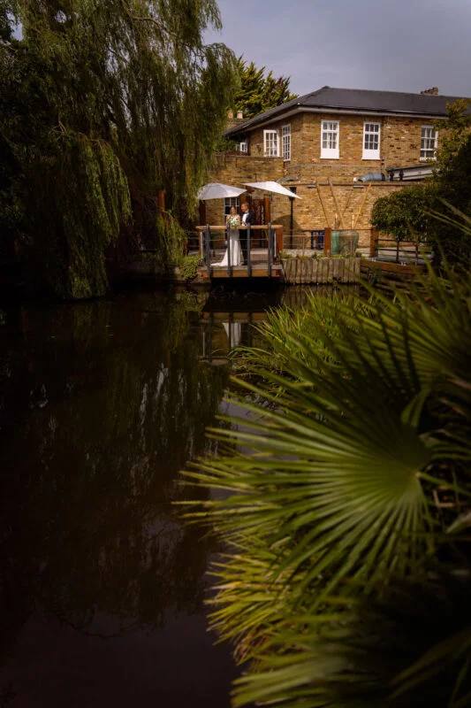 A bride and groom standing next to a pond.