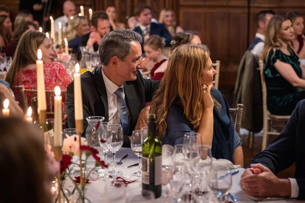 Guests enjoy a warm and lively wedding breakfast seated at candlelit banquet tables in a wood-panelled reception hall.