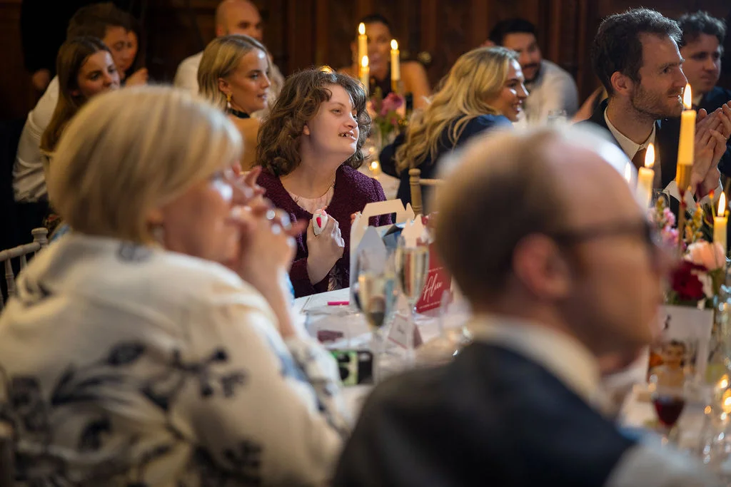 Wedding guests enjoy speeches and laughter around a candlelit dining table during the wedding reception.