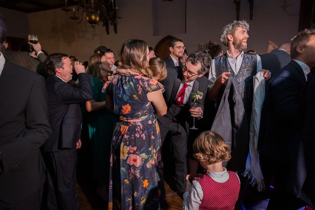 A lively candid shot captures wedding guests laughing and mingling during the evening reception in a historic venue.