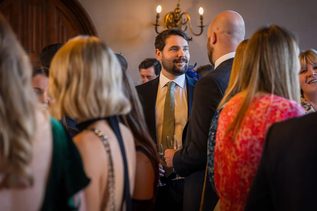 Wedding guests mingling and chatting animatedly during the drinks reception in a bright indoor venue.