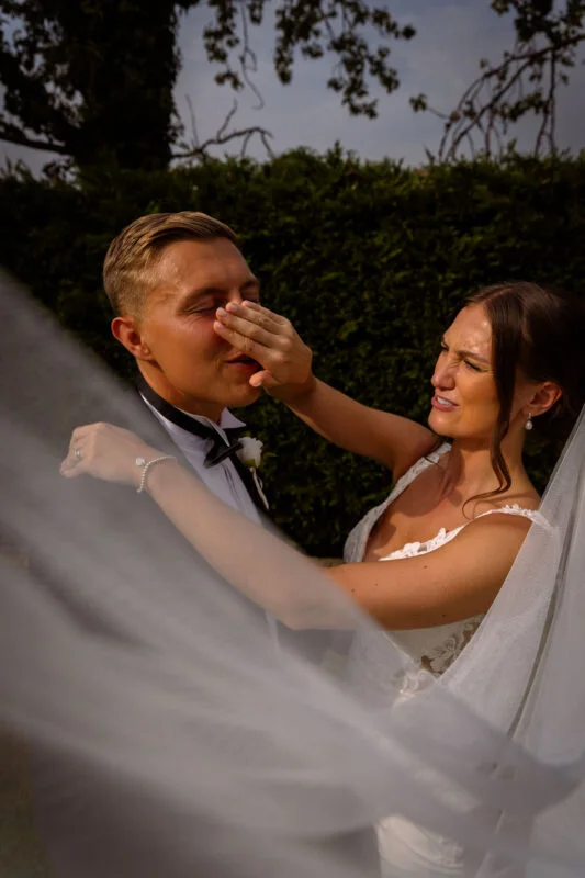 A bride and groom kissing in front of a veil.