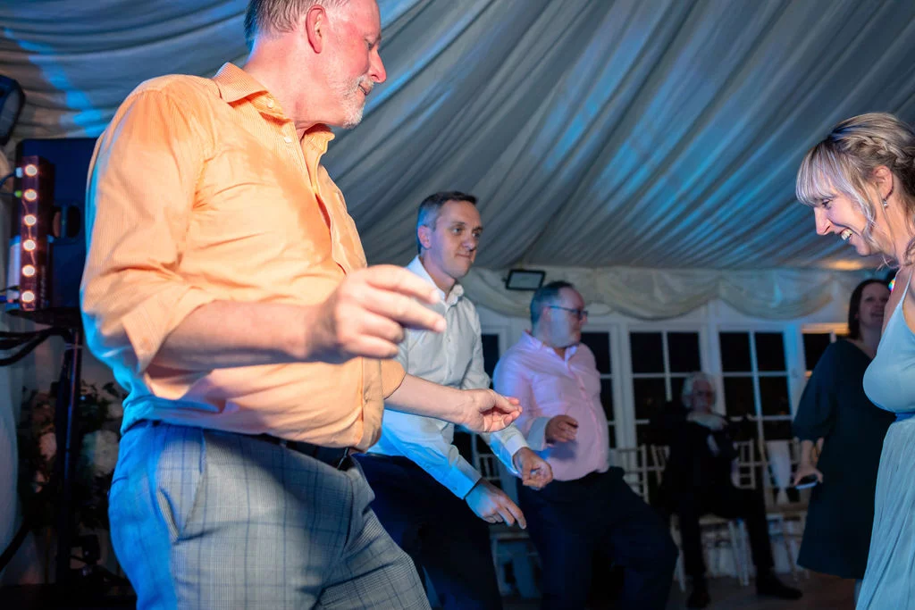 Guests enjoy dancing together inside a marquee decorated with pleated ceiling drapes and vibrant party lighting.
