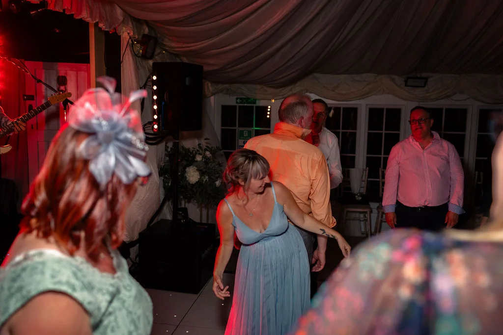 Wedding guests enjoy dancing and socialising inside an illuminated marquee during the lively evening reception.
