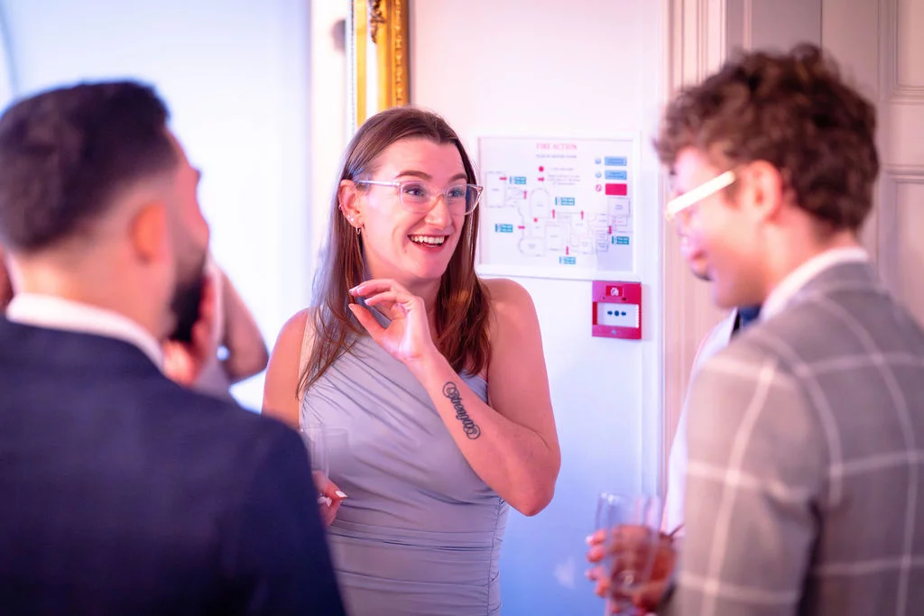 Wedding guests laugh and mingle together during a drinks reception, holding glasses and enjoying a relaxed moment.