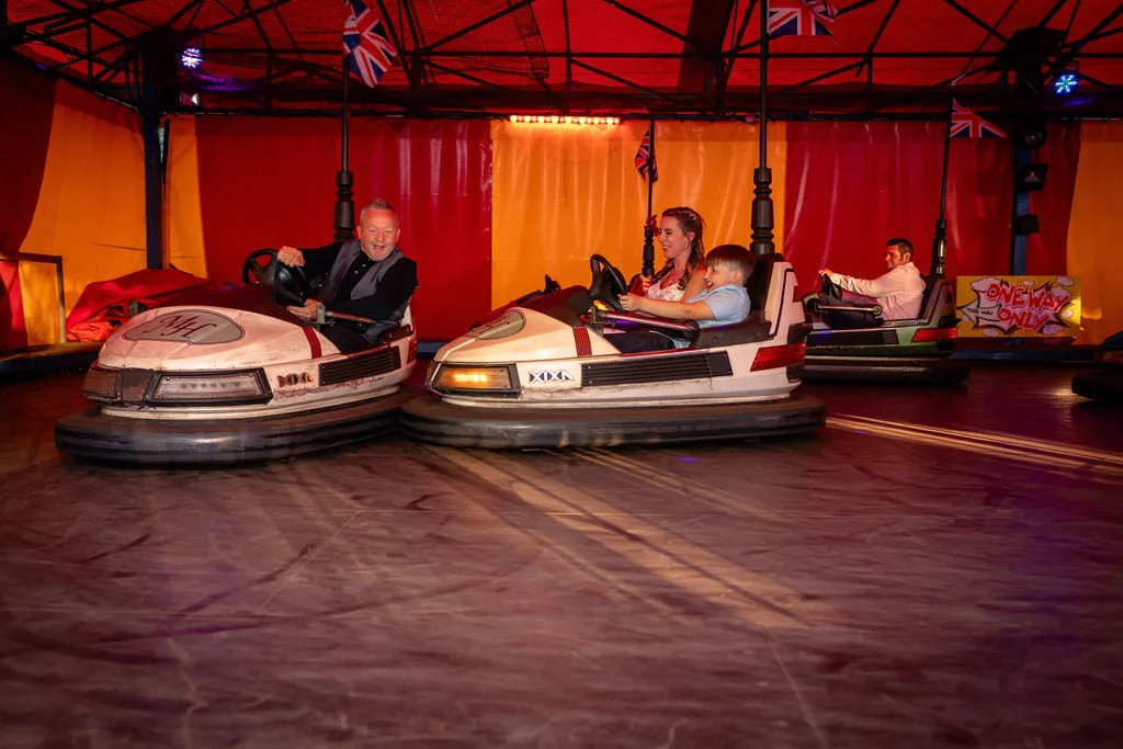 Wedding guests enjoy riding vintage bumper cars at a lively fairground-themed evening reception.