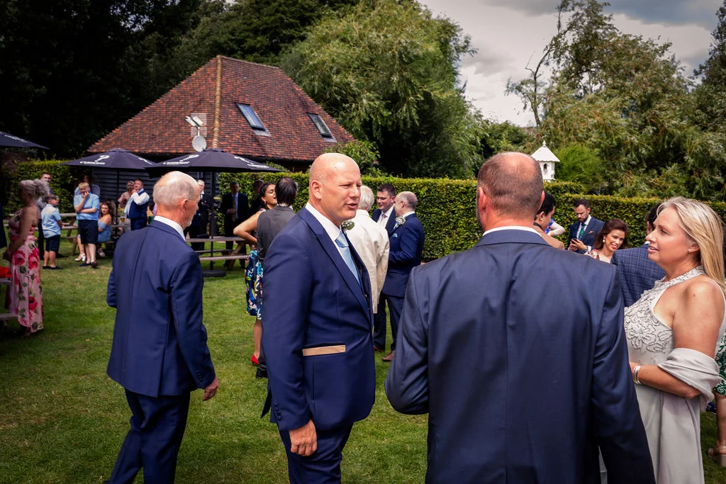 Wedding guests mingling and chatting on the lawn during the drinks reception outside a rustic country venue.