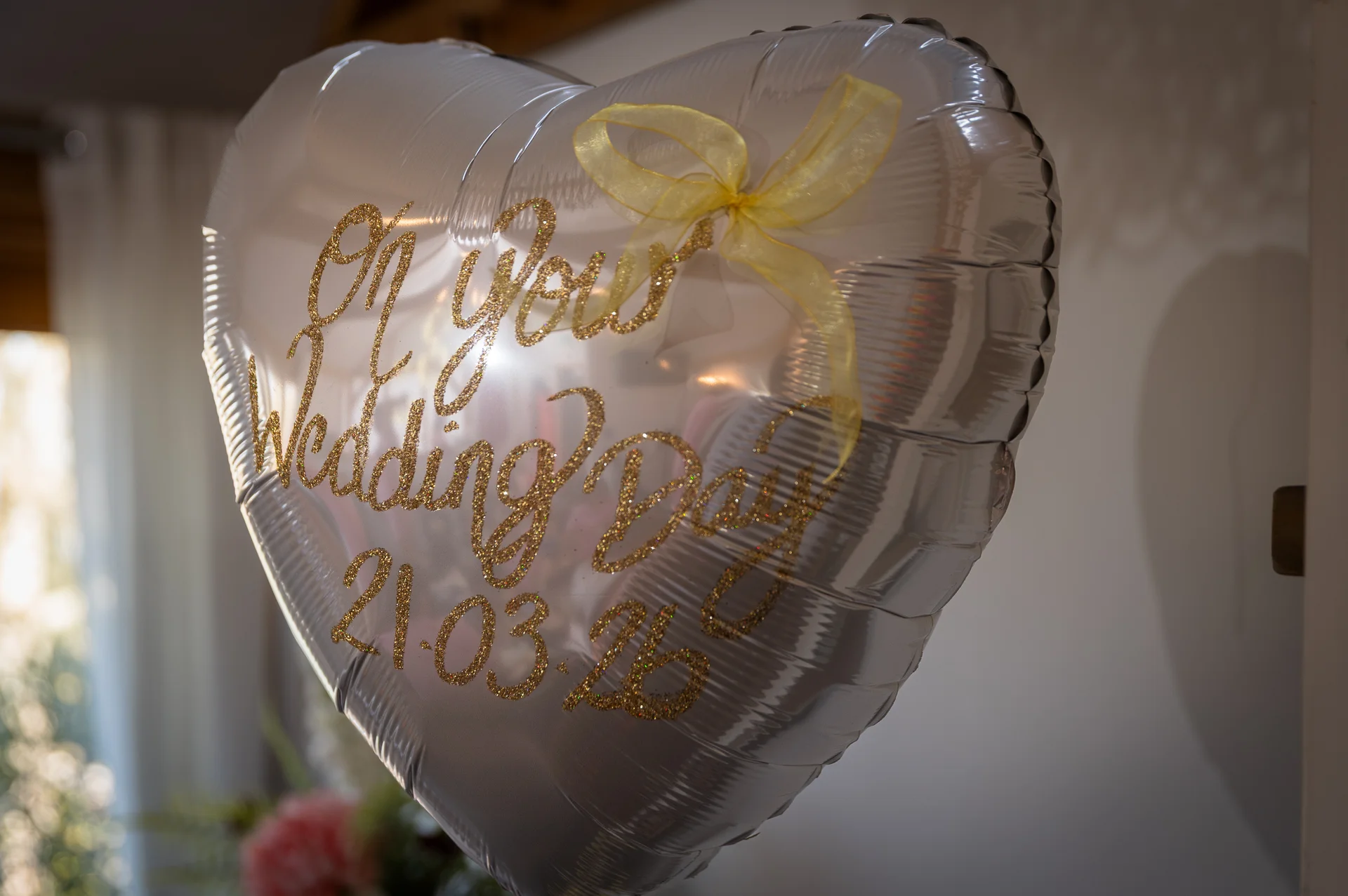 A silver heart-shaped foil balloon features gold glitter calligraphy reading on your wedding day with a date and a yellow ribbon bow.