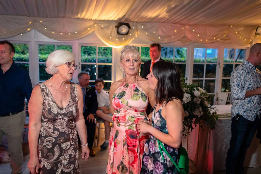 Guests mingle and chat during an evening reception inside a marquee decorated with draped fabric and fairy lights.