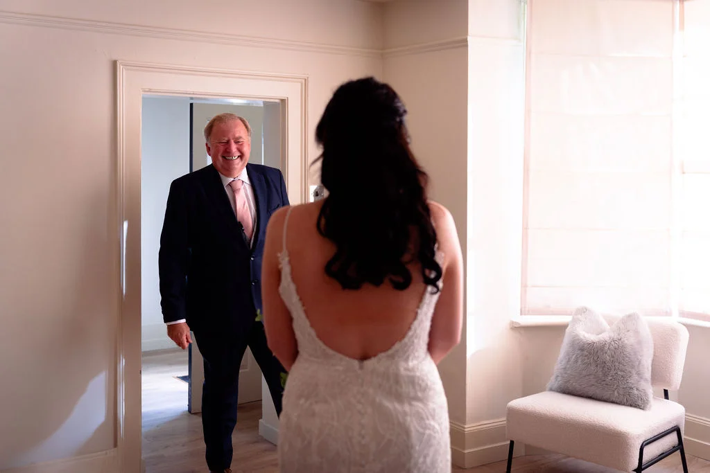 A smiling father beams with joy as he sees his daughter in her wedding dress during an emotional first look.