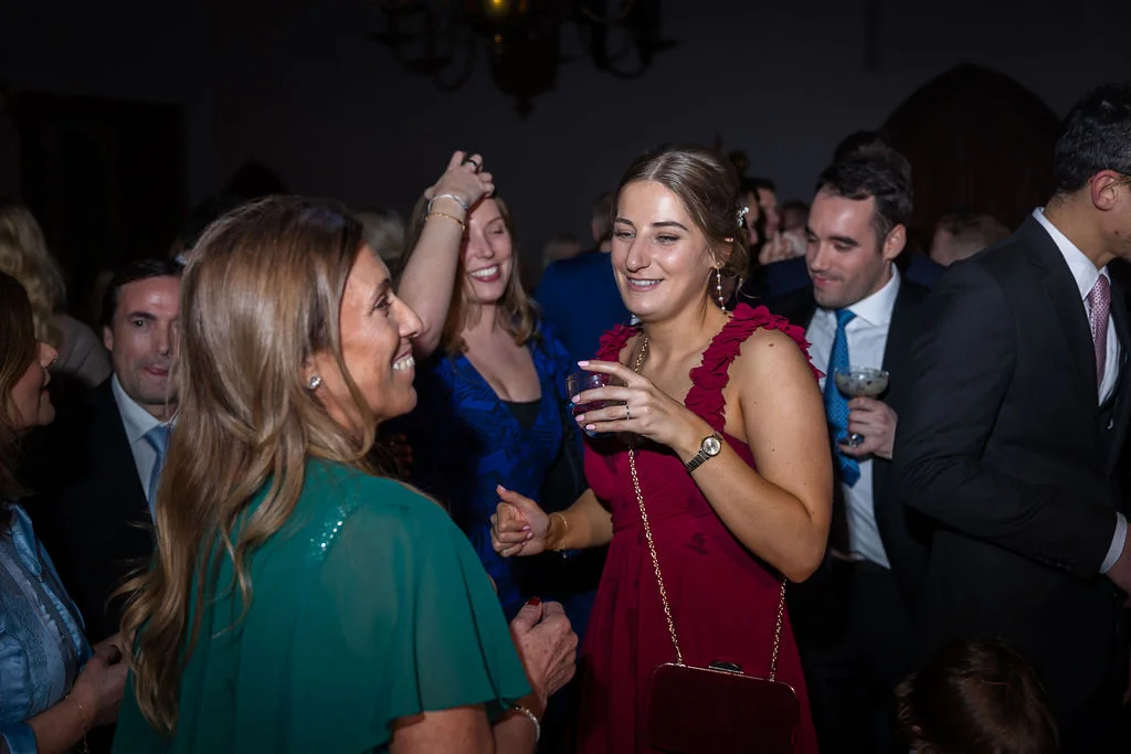 Wedding guests enjoy a lively evening reception, mingling and holding drinks under direct flash lighting.