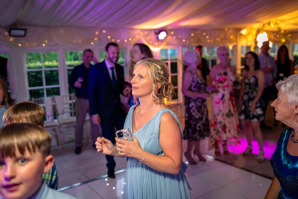 Guests enjoy the vibrant atmosphere on the illuminated dance floor inside a decorated marquee during the evening wedding reception.