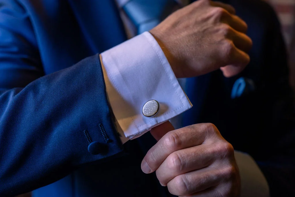A close-up shot of a groom in a navy suit adjusting his white shirt cuff and personalised silver cufflinks during morning preparations.