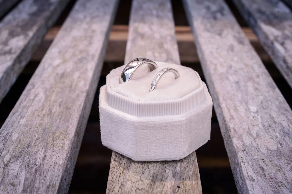Two polished silver wedding bands rest neatly inside an elegant white velvet octagonal ring box placed on a rustic wooden plank surface.