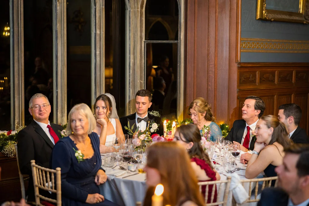 Newlyweds and family members enjoy a sophisticated wedding breakfast seated around a candlelit top table in a wood-panelled stately home.