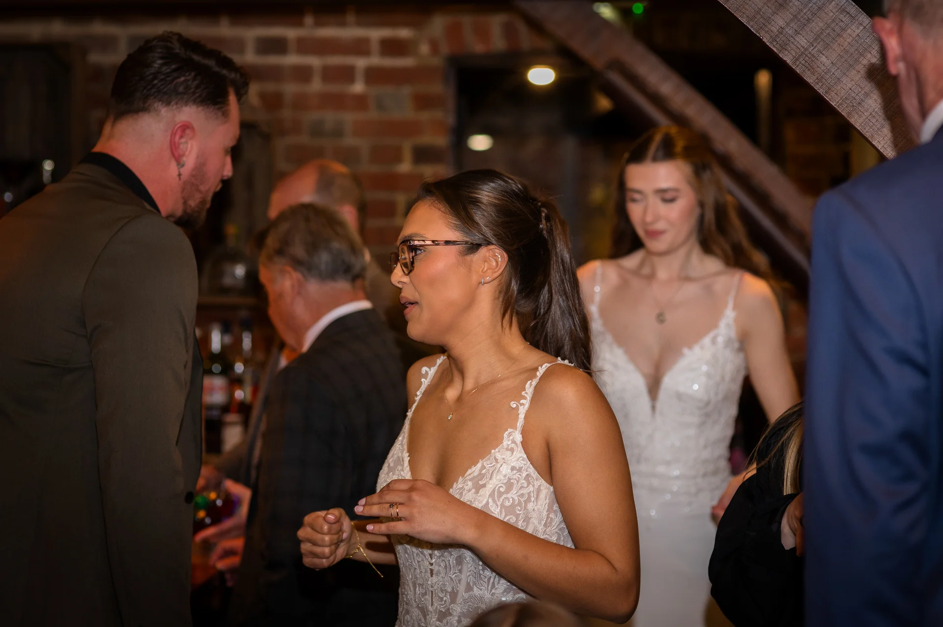 Wedding guests mingling and chatting in an intimate indoor reception venue with exposed brick walls.