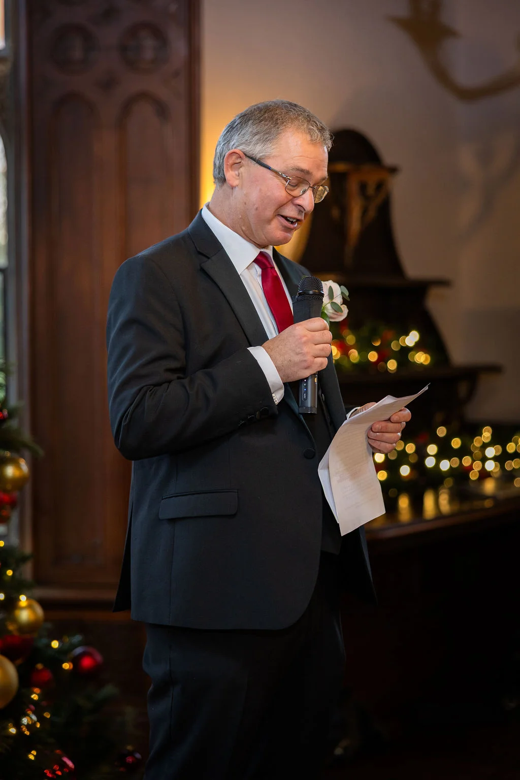 A father of the bride delivers a speech holding a microphone and notes during a festive Christmas wedding celebration.