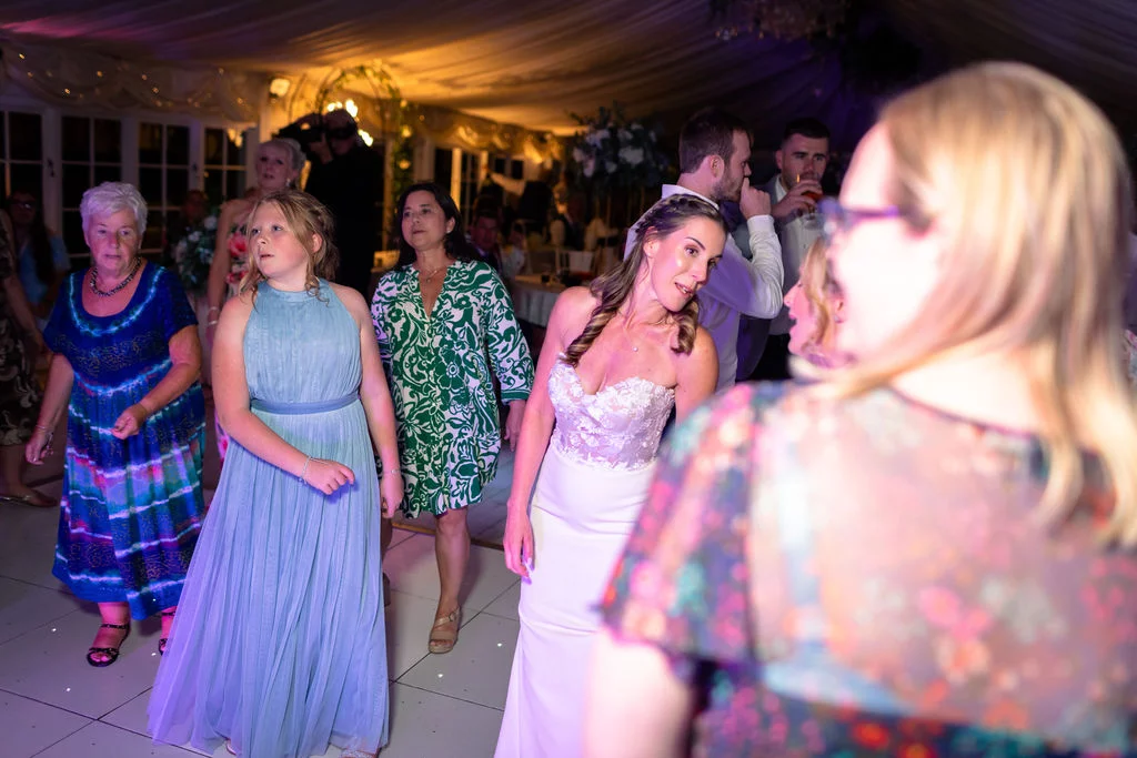 A lively evening reception inside a marquee where guests and the bride are dancing joyfully on the dance floor.