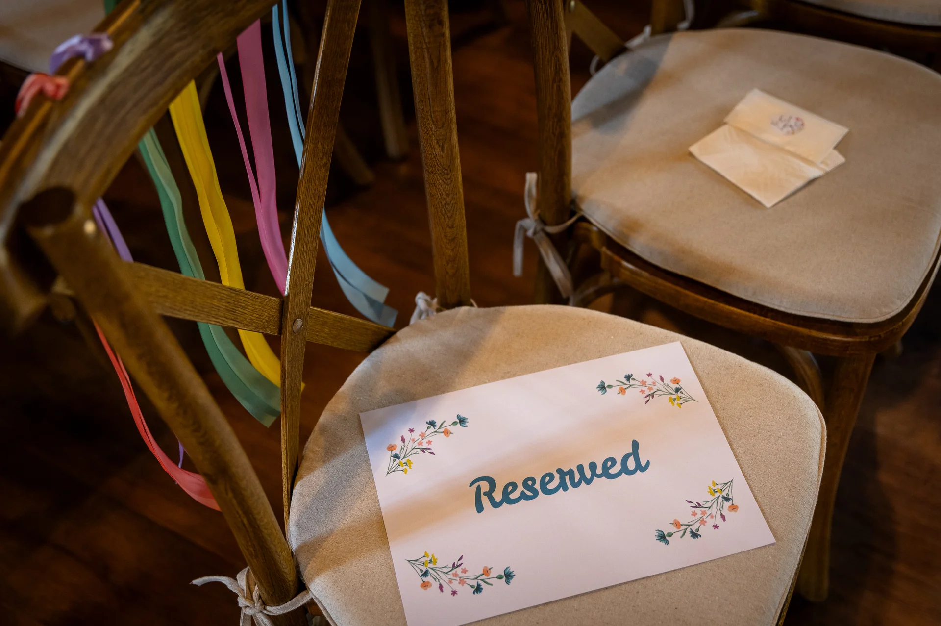 A reserved sign with floral illustrations rests on a padded wooden wedding chair decorated with colourful ribbons.