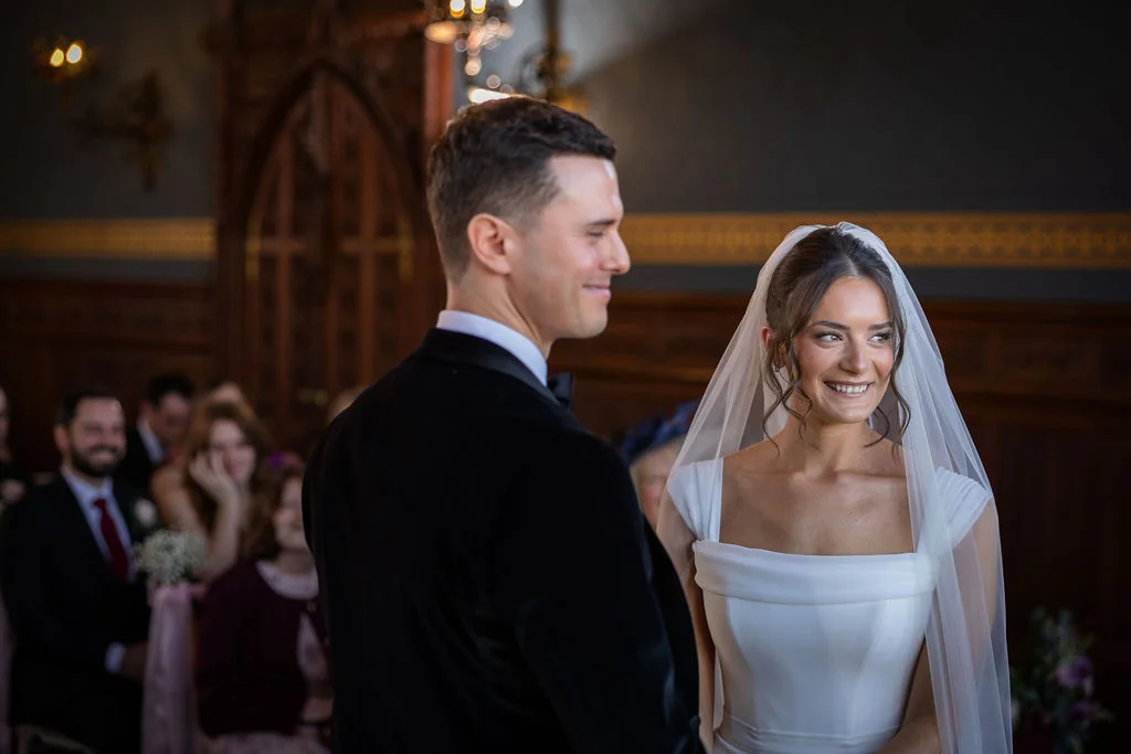 A smiling bride and groom share a joyful glance during their indoor civil ceremony in an elegant panelled room.