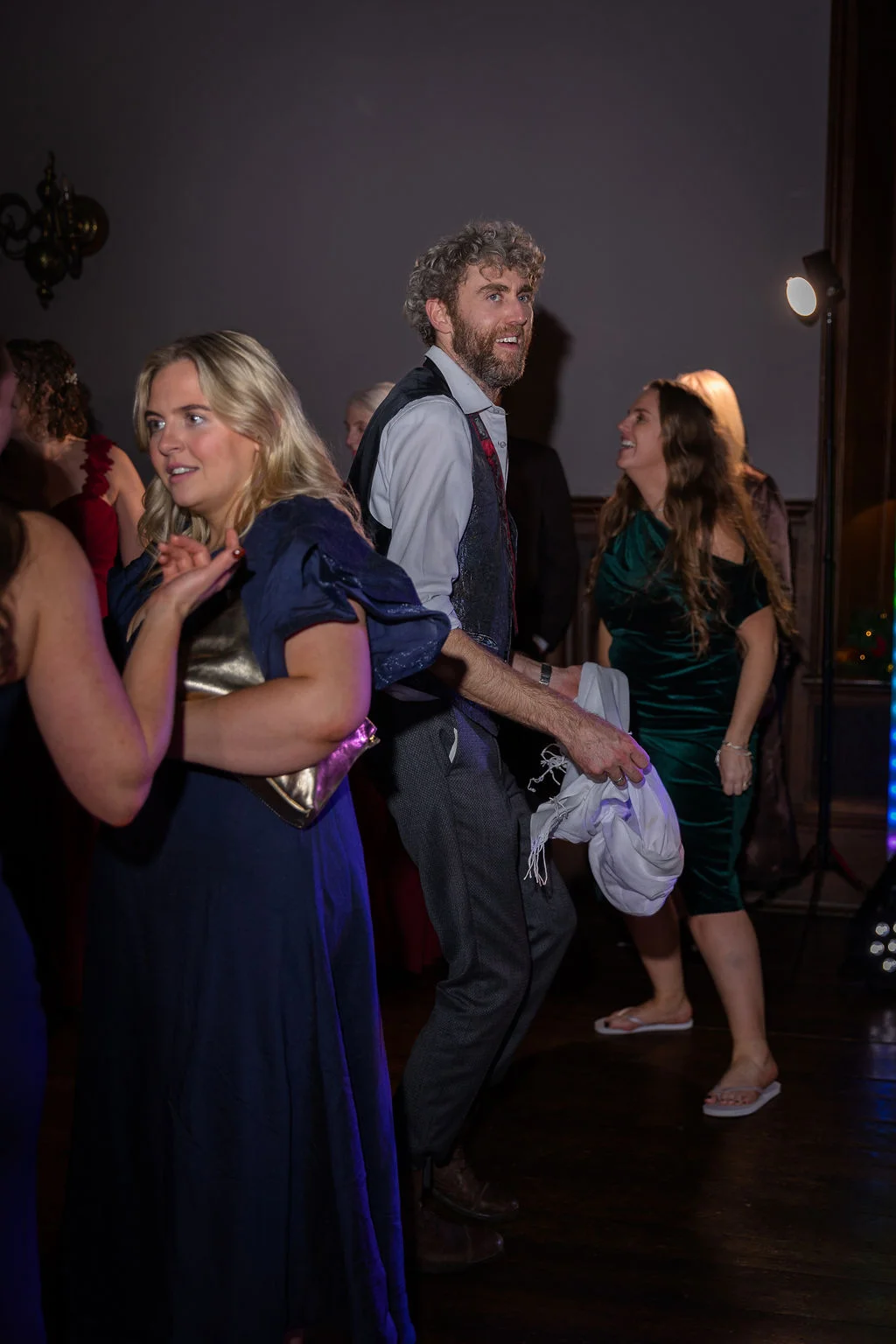 Wedding guests enjoy themselves dancing energetically on a wooden floor at the evening reception.