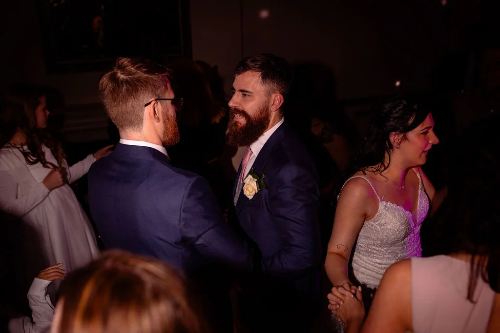 The bride and groom share a joyful moment dancing together at their evening wedding reception surrounded by guests.