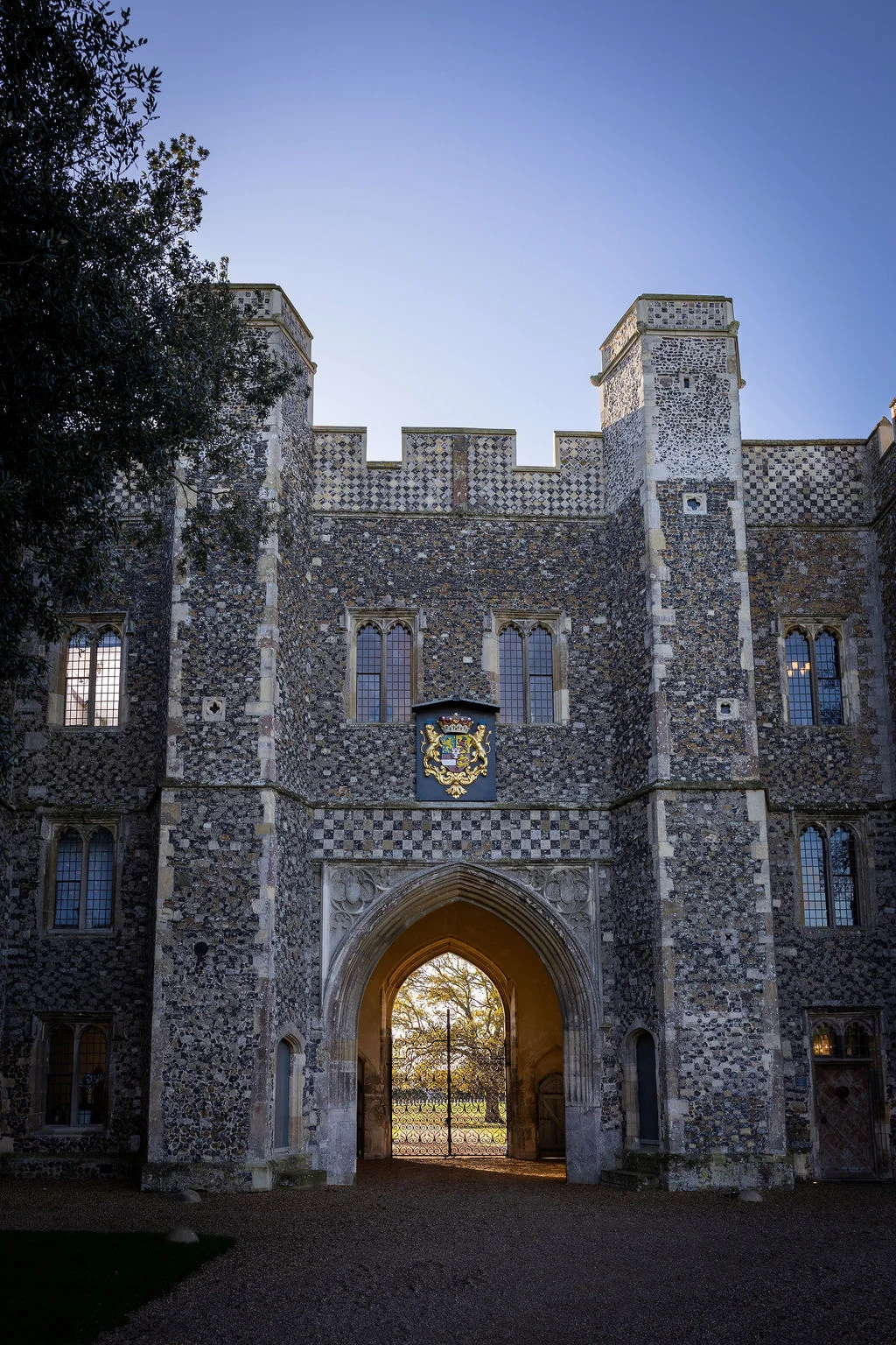 A magnificent historic stone castle facade featuring a grand central arched gateway and decorative heraldry under a clear blue sky.