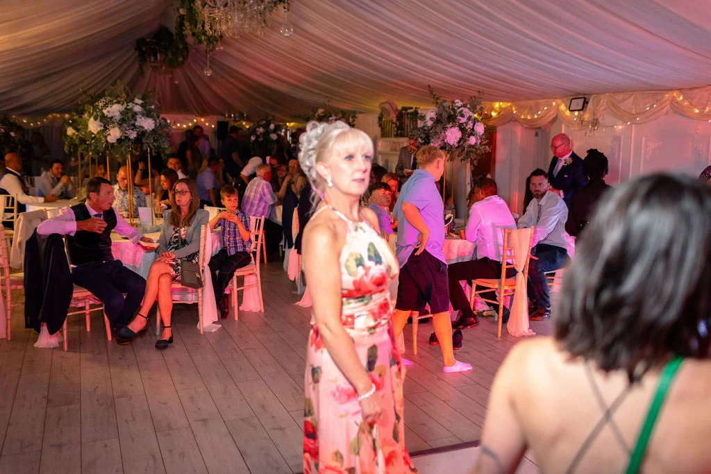 Guests mingling inside a beautifully draped marquee illuminated with fairy lights during a wedding evening reception.