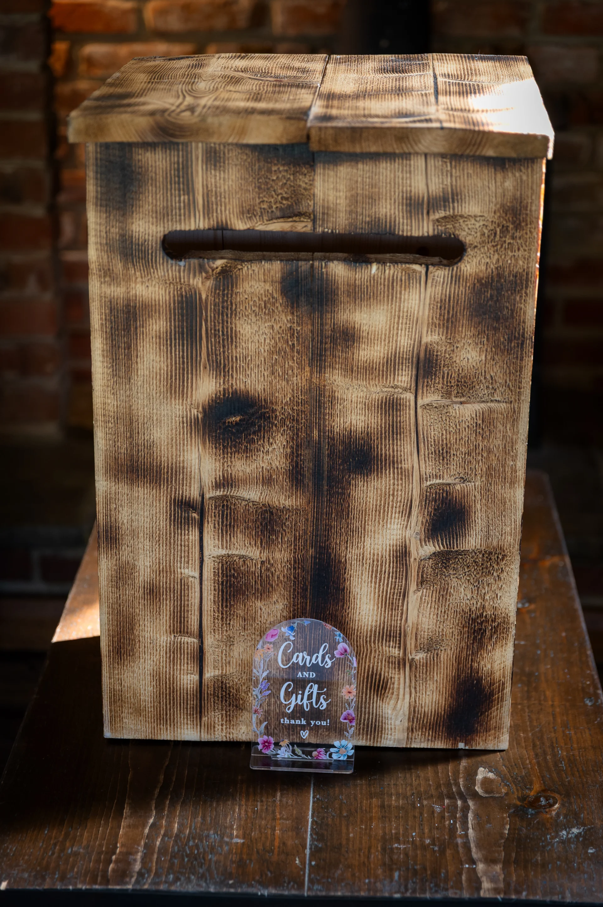 A rustic wooden wedding card box sits on a wooden table with a floral acrylic sign reading cards and gifts.