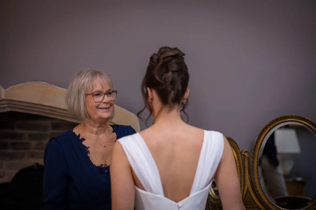 An emotional mother of the bride looks admiringly at her daughter in her wedding dress during morning preparations.