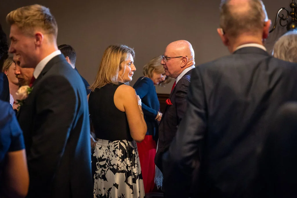 Wedding guests wearing formal attire mingle and converse naturally during a lively evening reception gathering.