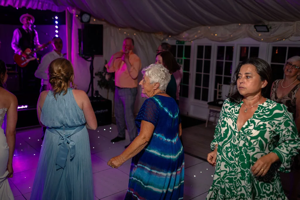 Guests enjoy dancing on an illuminated dance floor inside a decorated marquee with a live band performing in the background.