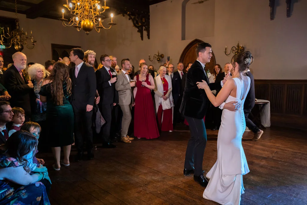 The newlywed couple share their first dance in a grand stately home ballroom while guests watch from the sidelines.