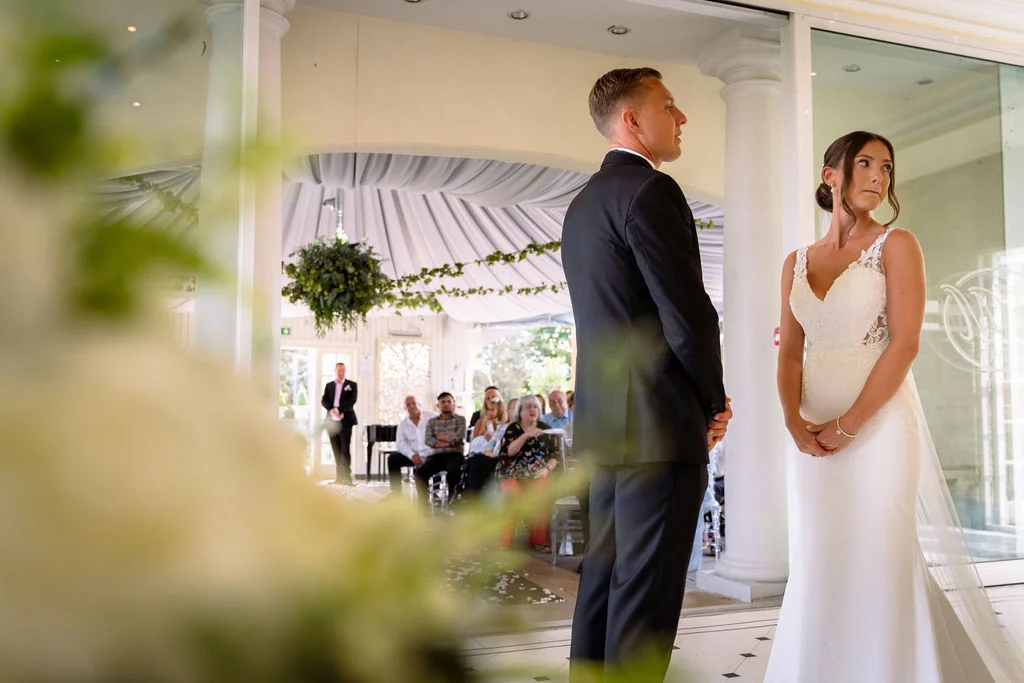 A bride and groom stand in front of a glass door.