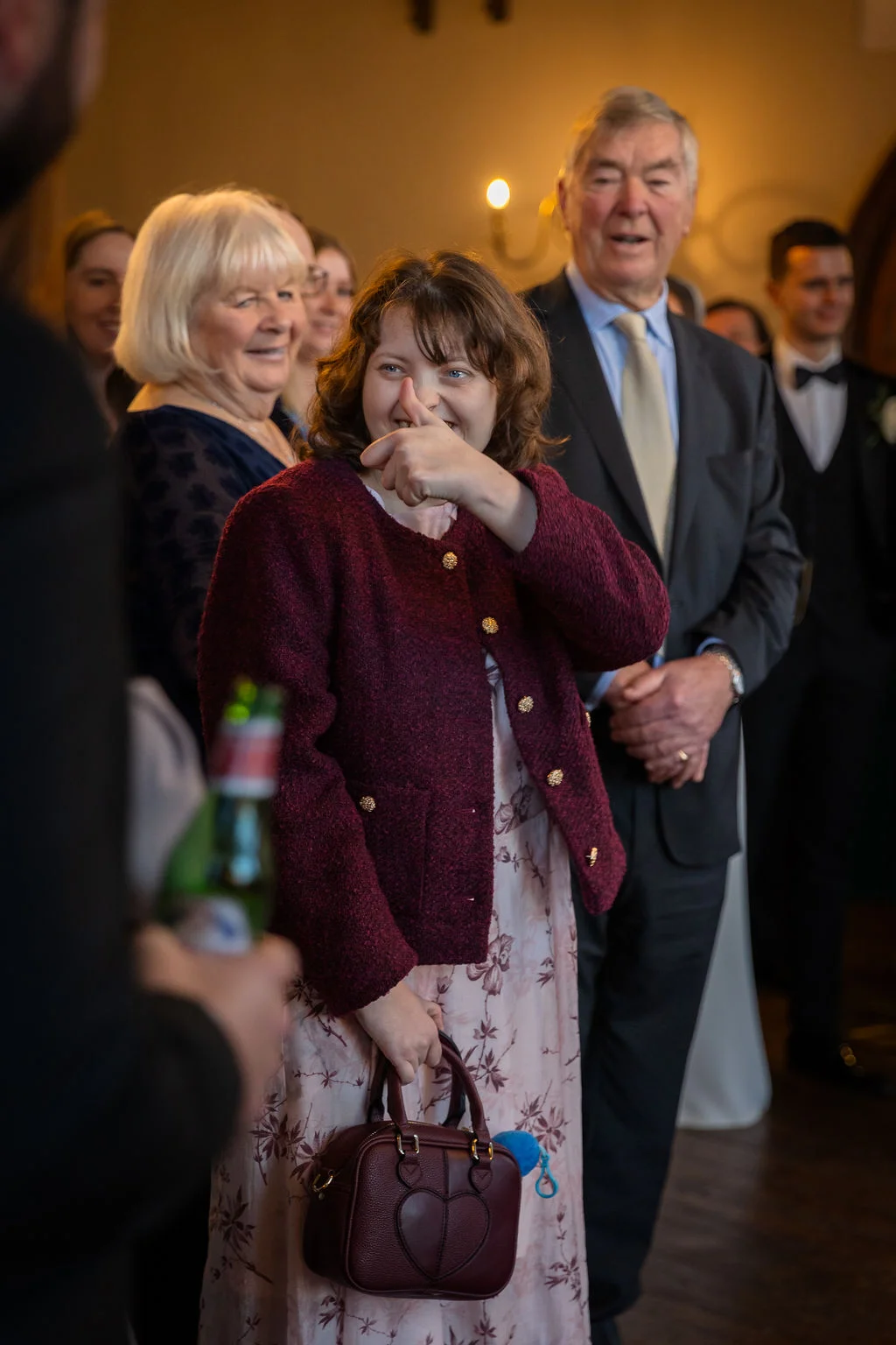 A joyful wedding guest laughs and points cheerfully while surrounded by family members during the indoor reception celebrations.