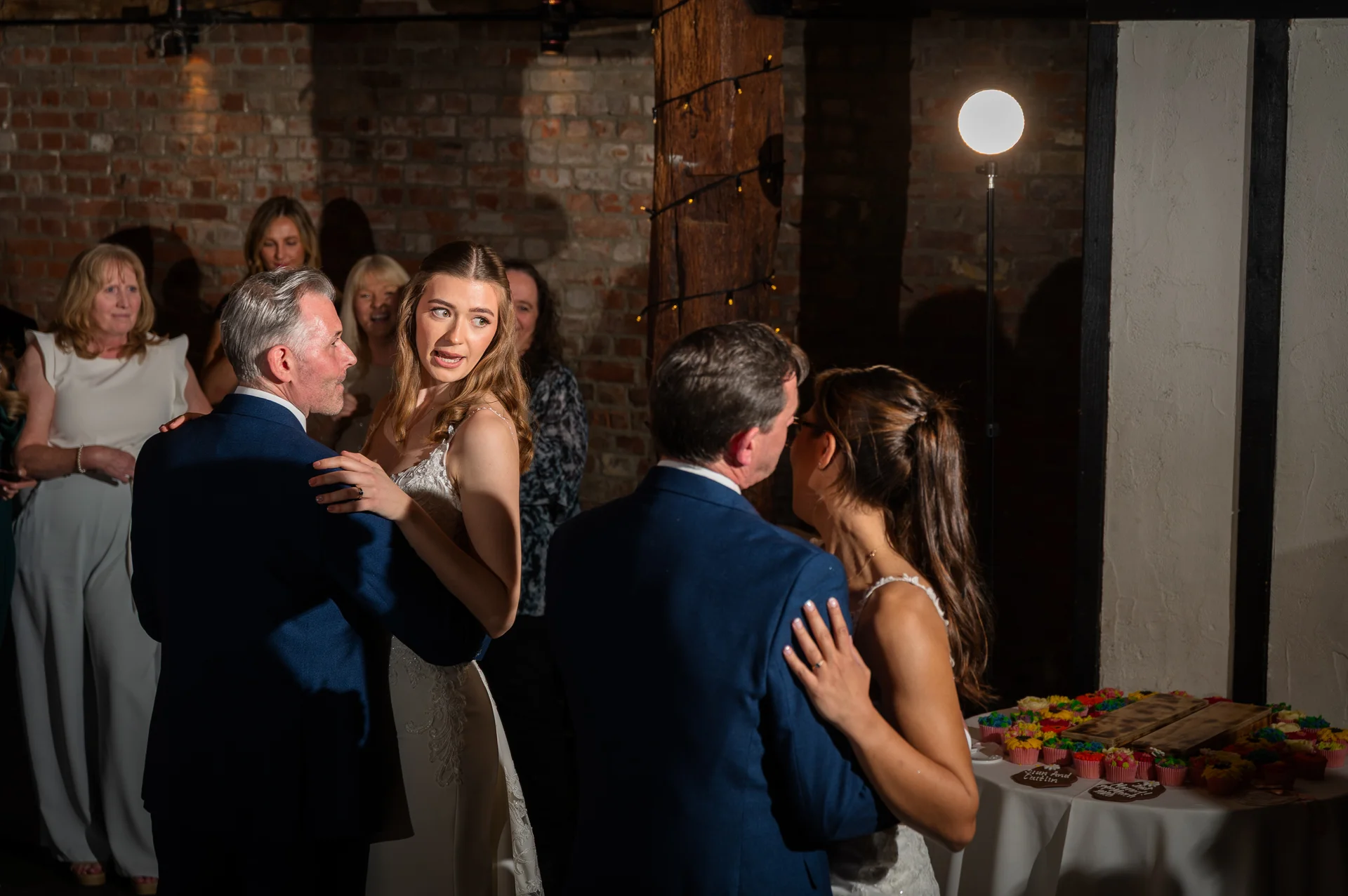Two couples share a joyful first dance inside a rustic brick barn during the evening reception, illuminated by direct flash lighting.
