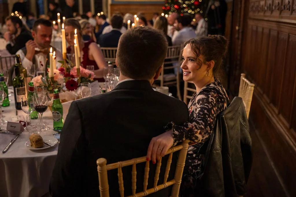 A guest looks smilingly across a candlelit wedding reception table towards a companion during the wedding breakfast.
