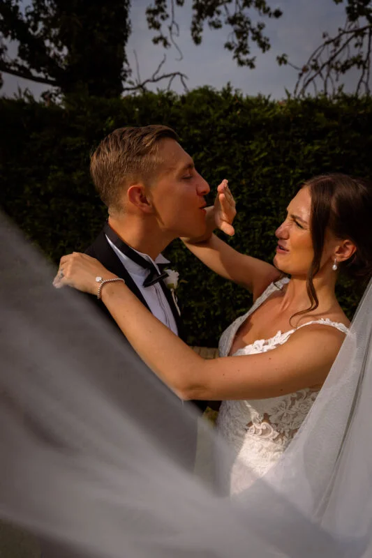 A bride and groom kissing in front of a veil.